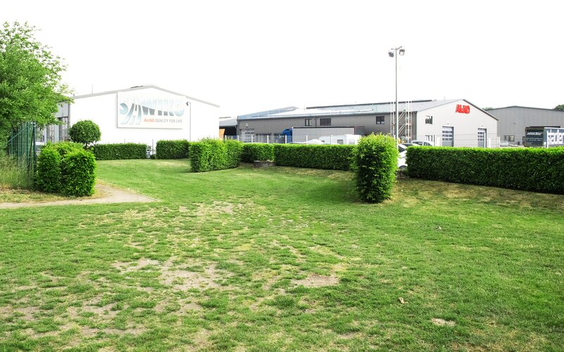 Caravan pitch bordered by a green hedge, with the AL-KO Customer Center building in the background | © AL-KO Vehicle Technology Group