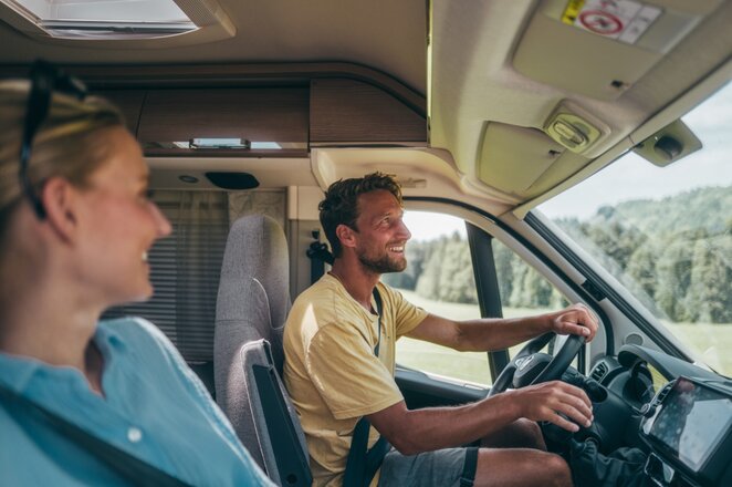 A man is driving a motorhome, a woman sits in the passenger seat. Both are laughing. | © AL-KO