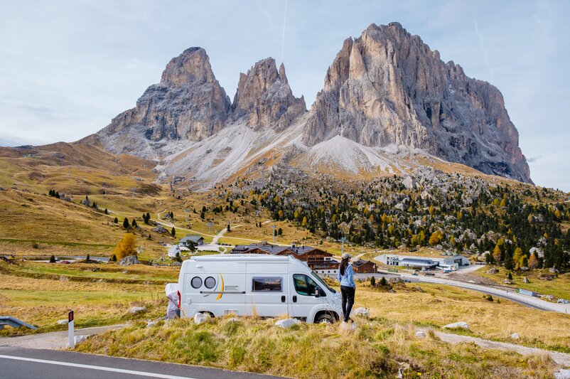 A woman stands beside her camper van at the roadside, looking towards The Three Peaks.