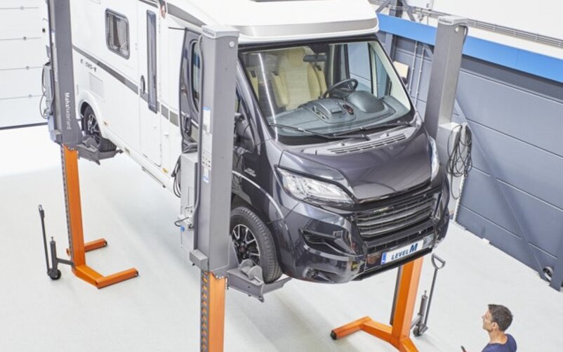 From the installation of automatic levelling systems to track measurement, you can rest assured that your camping vehicle is in good hands at the Benelux customer centre. | © AL-KO A mechanic standing in front of a car lift with a motorhome raised on it | © AL-KO