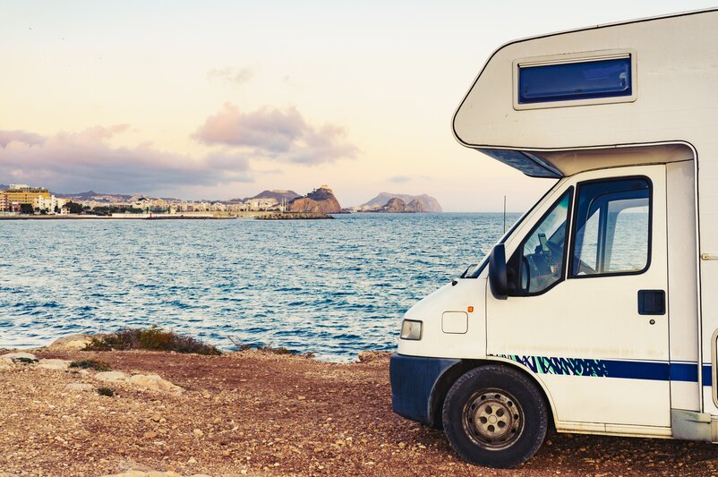 Motorhome parked with a view of the sea and a coastal city.