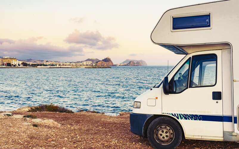 Motorhome parked with a view of the sea and a coastal city.