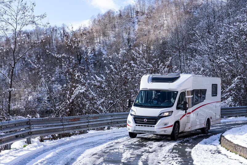 A camper van driving around a bend on a snow-covered road.