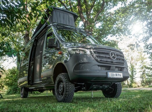 Mercedes-Benz Sprinter camper van with pop-up roof, parked on a grassy area under trees in sunny weather. | © AL-KO VT